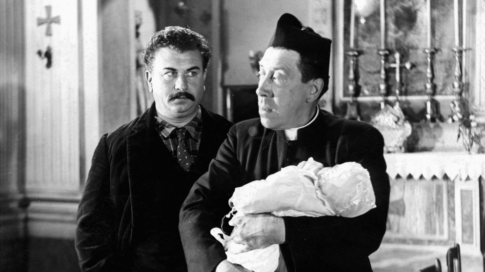 Don Camillo (Fernandel, rechts) weigert sich, das Baby seines Lieblingsfeindes Peppone (Gino Cervi) zu taufen. | Bildquelle: ARD Degeto