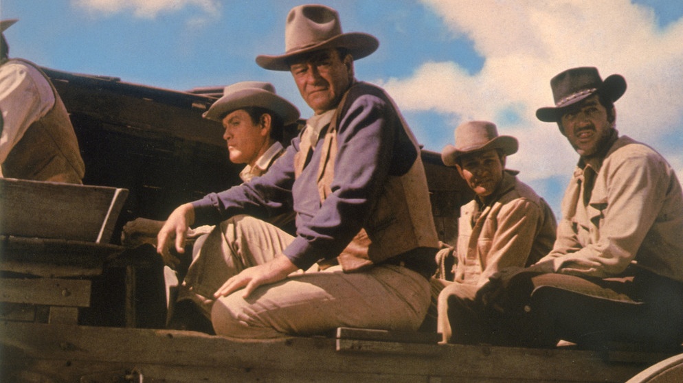 Die Söhne der Katie Elder – John (John Wayne, zweiter von links), der älteste und ein Revolverheld; Tom (Dean Martin, rechts), ein professioneller Spieler; Matt (Earl Holliman, zweiter von rechts), ein erfolgloser Eisenwarenhändler; und der jüngste, Bud (Michael Anderson Jr., links) – waren jahrelang nicht mehr zu Haus und sind zur Beerdigung angereist. Doch die Bewohner von Clearwater stehen ihnen recht ablehnend gegenüber, da sie sich nicht sehr um ihre Mutter gekümmert hatten. | Bildquelle: BR/Paramount Pictures