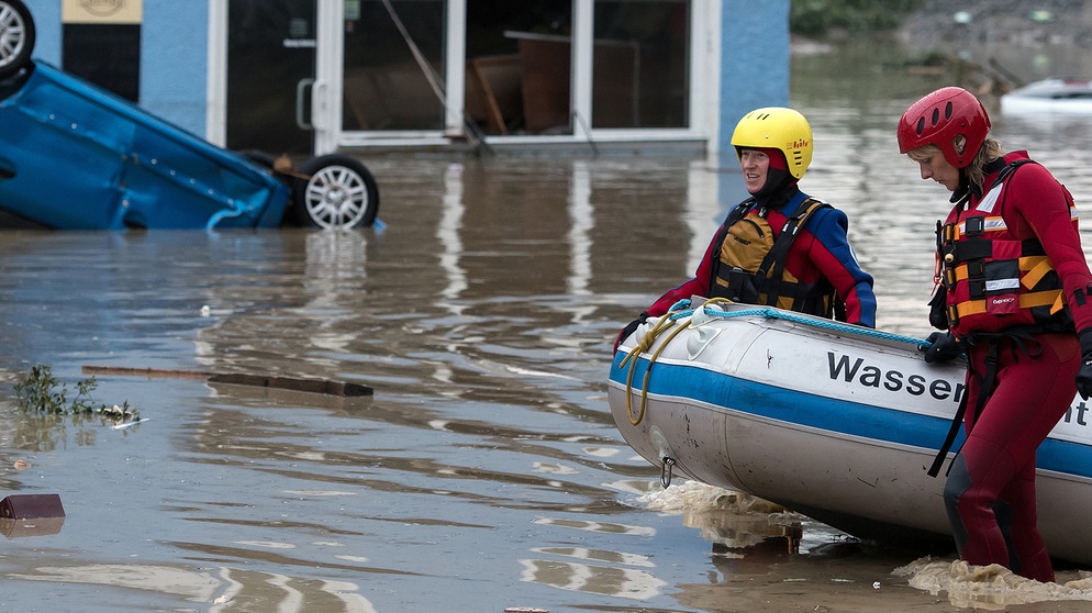 Mitarbeiterinnen der Wasserwacht ziehen am 01.06.2016 in Simbach am Inn (Landkreis Rottal-Inn) ein Schlauchboot durch das Hochwasser während im Hintergrund ein Auto kopfüber in den Fluten liegt. Nach anhaltendem Dauerregen ist ein Teil des Landkreises Rottal-Inn in Bayern am Mittwoch überschwemmt worden. Foto: Sven Hoppe/dpa | Bildquelle: picture alliance / dpa | Sven Hoppe