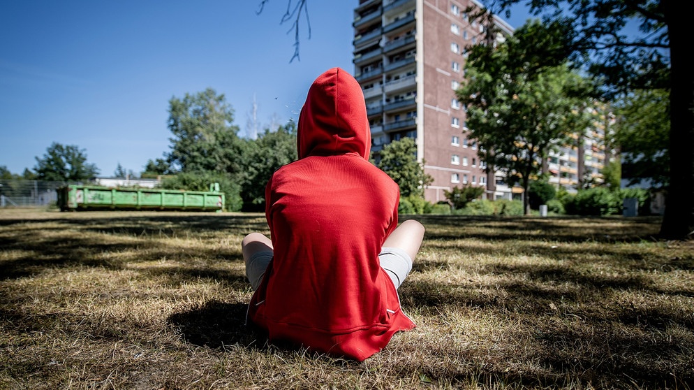 Jugendlicher sitzt im Rasen vor einem Plattenbau | Bildquelle: picture alliance / ZB | Thomas Eisenhuth