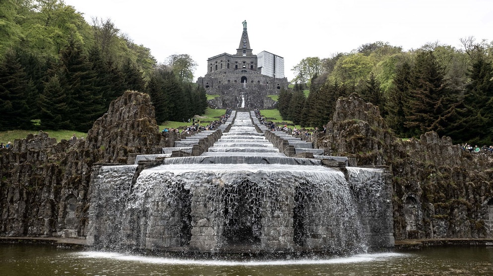 Besucher stehen bei den Wasserspielen im UNESCO-Welterbe Bergpark Wilhelmshöhe an den Kaskaden unterhalb des Herkules-Denkmals. | Bildquelle: picture alliance/dpa | Swen Pförtner