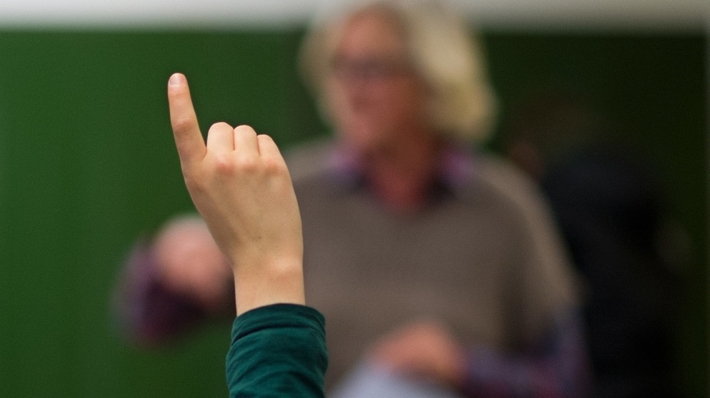 Lehrer im Unterricht vor grüner Tafel, ein Schüler hebt den Finger | Bildquelle: dpa-Bildfunk/Julian Stratenschulte