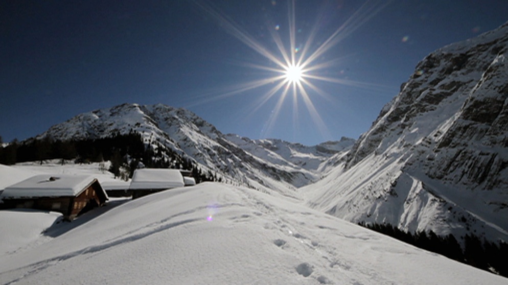 Unter unserem Himmel - Winter im Lechtal: Schneebedeckte Berglandschaft mit kleinen Holzhütten; die strahlende Sonne scheint am blauen Himmel | Bildquelle: BR